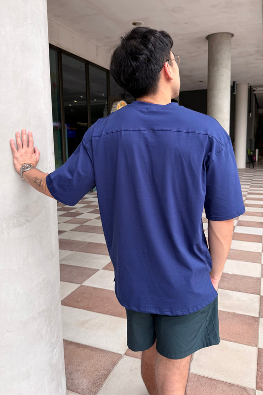 Person wearing a navy blue shirt and dark shorts standing against a white column in an indoor setting.