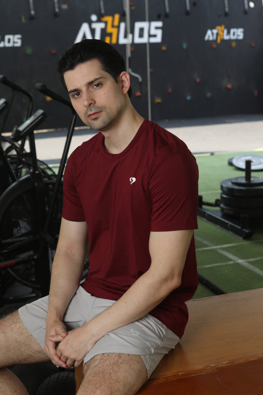 Man sitting on a bench in a gym in maroon everyday tshirt - Sandactive