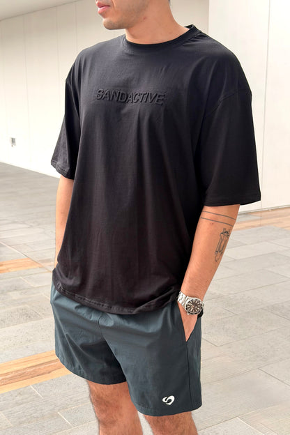 Person wearing a black t-shirt with 'SandActive' text and dark shorts indoors.