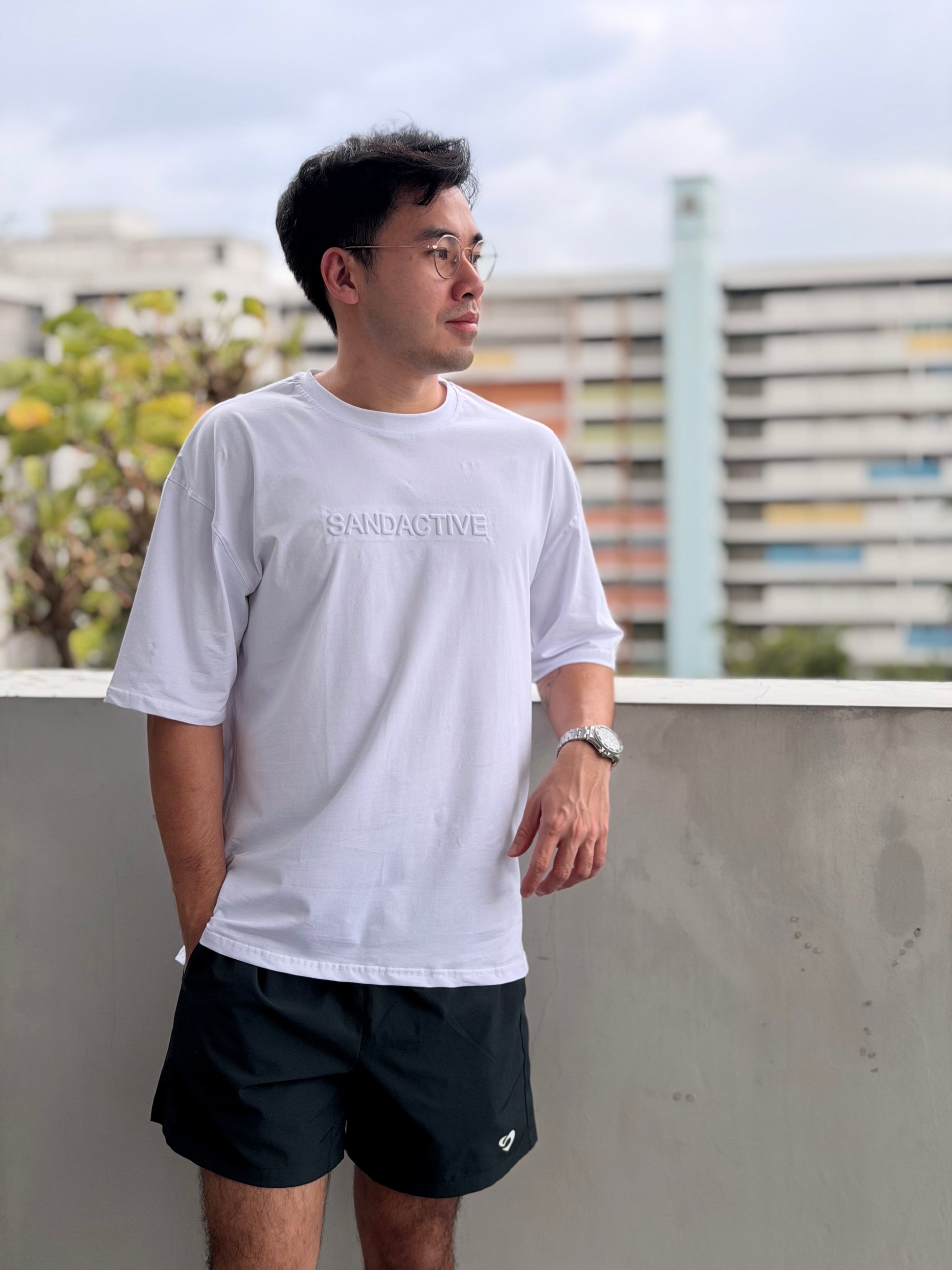 Man wearing a white t-shirt with text and black shorts standing outdoors.