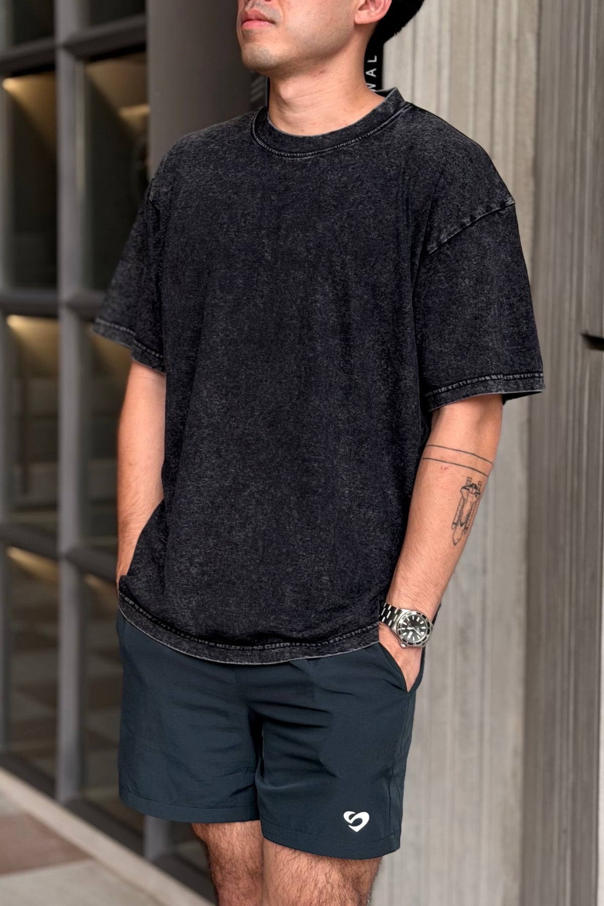 Man wearing a vintage oversized black t-shirt and shorts standing against a modern building.