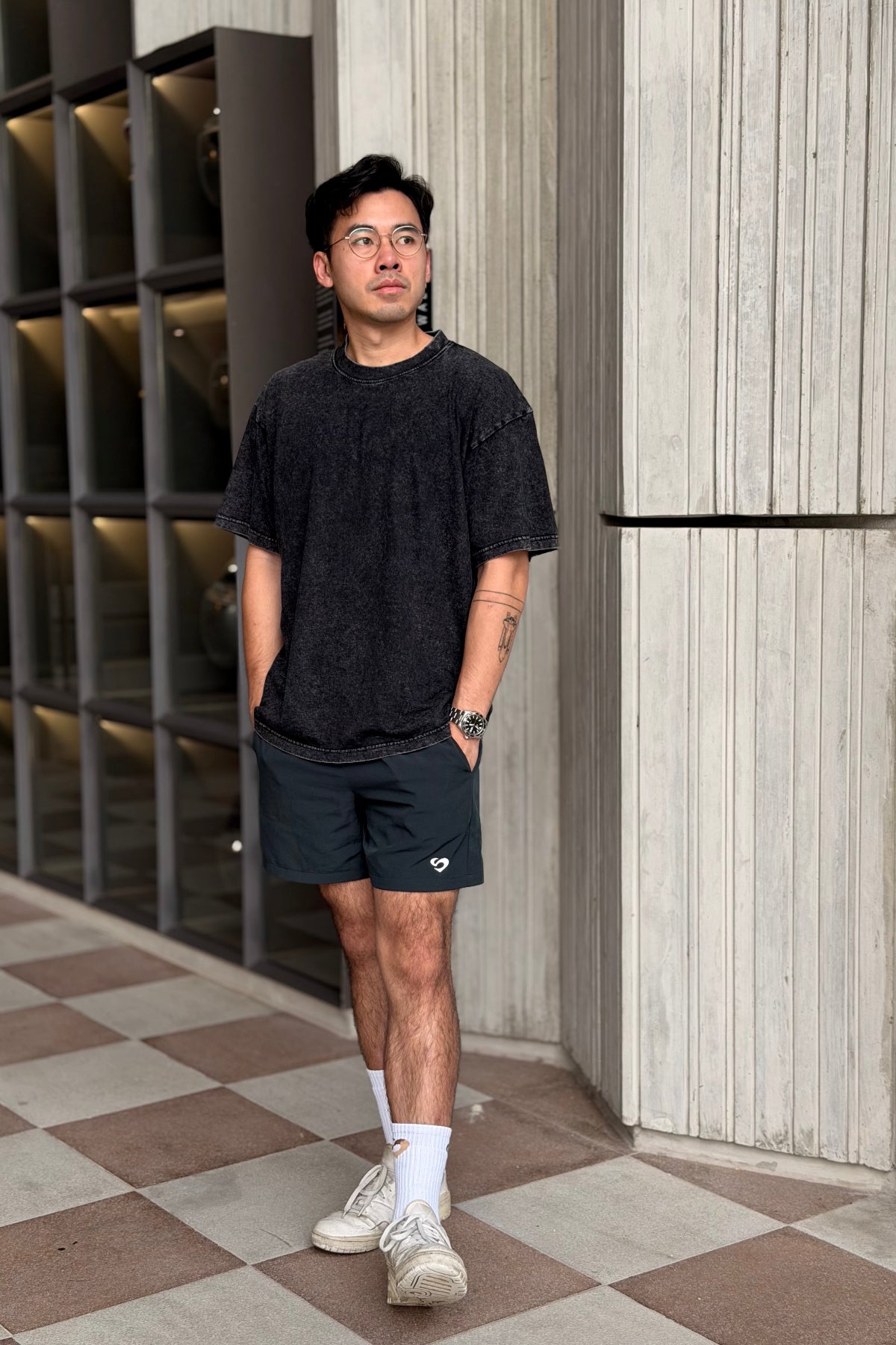 Man wearing a vintage oversized black t-shirt and shorts standing in front of a modern building.