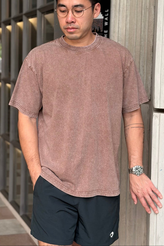 Man wearing a vintage oversized coffee t-shirt and forest green everyday shorts standing against a textured wall.