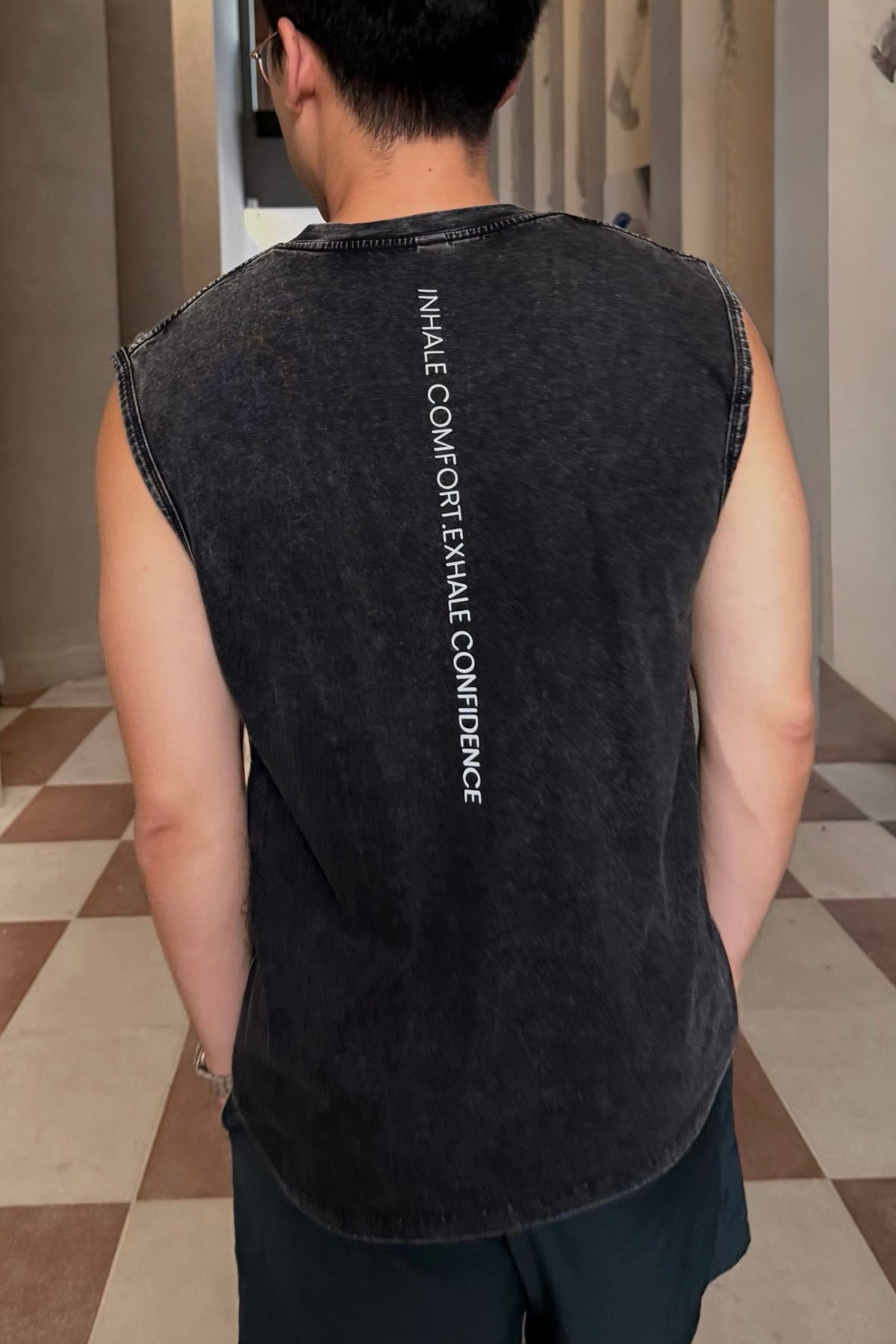 Person wearing a black sleeveless shirt with text walking down a hallway.